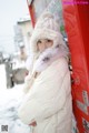 A woman in a white coat and fur hat leaning against a red vending machine.