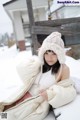 A woman sitting on a bench in the snow wearing a hat.