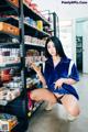 A woman in a blue shirt and black panties crouching down in a store.