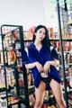 A woman in a blue shirt and black panties standing in front of a shelf of food.