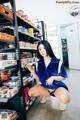 A woman in a blue shirt and black panties crouching down in a store.