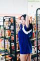 A woman in a blue dress standing in front of a shelf of food.