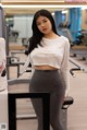 A woman in a white top and gray leggings standing in a gym.