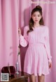 A woman in a pink dress standing next to a pink curtain.