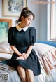 A woman sitting on a bed wearing a black dress.