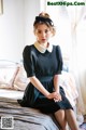 A woman sitting on a bed wearing a black dress.