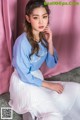 A woman sitting on the floor wearing a blue sweatshirt and white skirt.