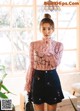 A woman in a pink blouse and black skirt posing for a picture.