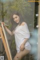 A woman in a white shirt is painting on a easel.