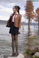 A woman in a school uniform standing on a rock by the water.