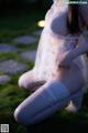 A woman in a white lingerie sitting on the grass.