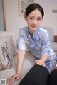 A woman in a blue and white cheongsam sitting on a couch.