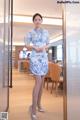 A woman in a blue and white dress standing in front of a glass door.