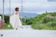 A woman in a white dress and straw hat walking down a road.