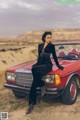 A woman sitting on top of a red car in the desert.