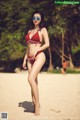 A woman in a red bikini standing on a beach.