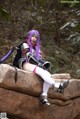 A woman with purple hair sitting on a rock.