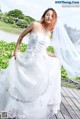 A woman in a wedding dress sitting on a wooden dock.