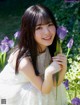 A woman in a white dress holding a purple flower.