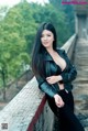 A woman in a black leather jacket leaning against a fence.