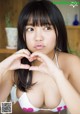 A woman in a white bikini making a heart with her hands.