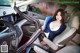 A woman sitting in the driver's seat of a car holding a book.