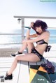 A woman in a bikini sitting on a boardwalk next to the ocean.