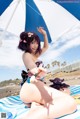 A woman in a bikini sitting under an umbrella on the beach.