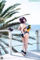 A woman in a bikini standing on a balcony next to the ocean.