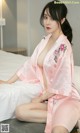 A woman in a pink robe sitting on a bed.